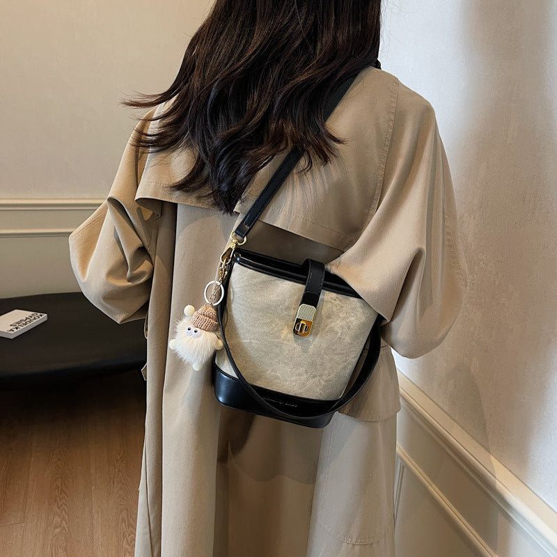 Vintage bucket crossbody bag in beige with black trim and gold buckle, featuring a fluffy charm.
