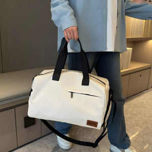 Creamy-white nylon travel duffel bag with black handles and adjustable strap, featuring a front zip pocket.