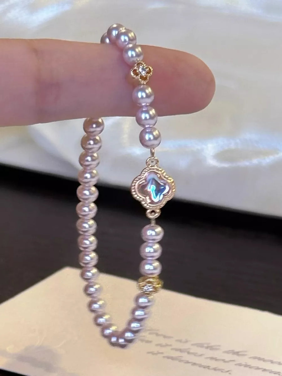 Delicate pearl bracelet with clover charm and gold accents.