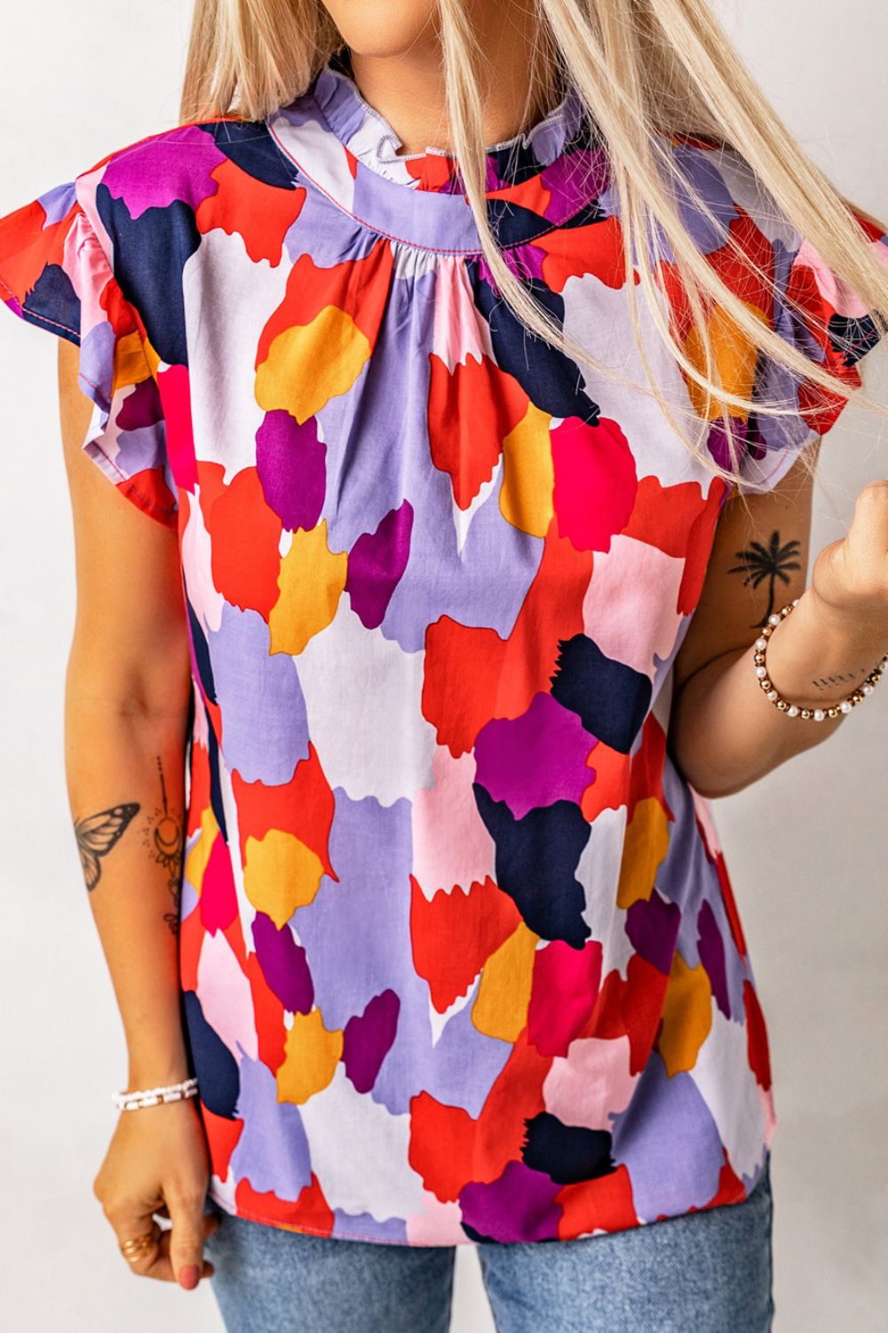 Blouse with abstract print, ruffle neck, and short flutter sleeves.