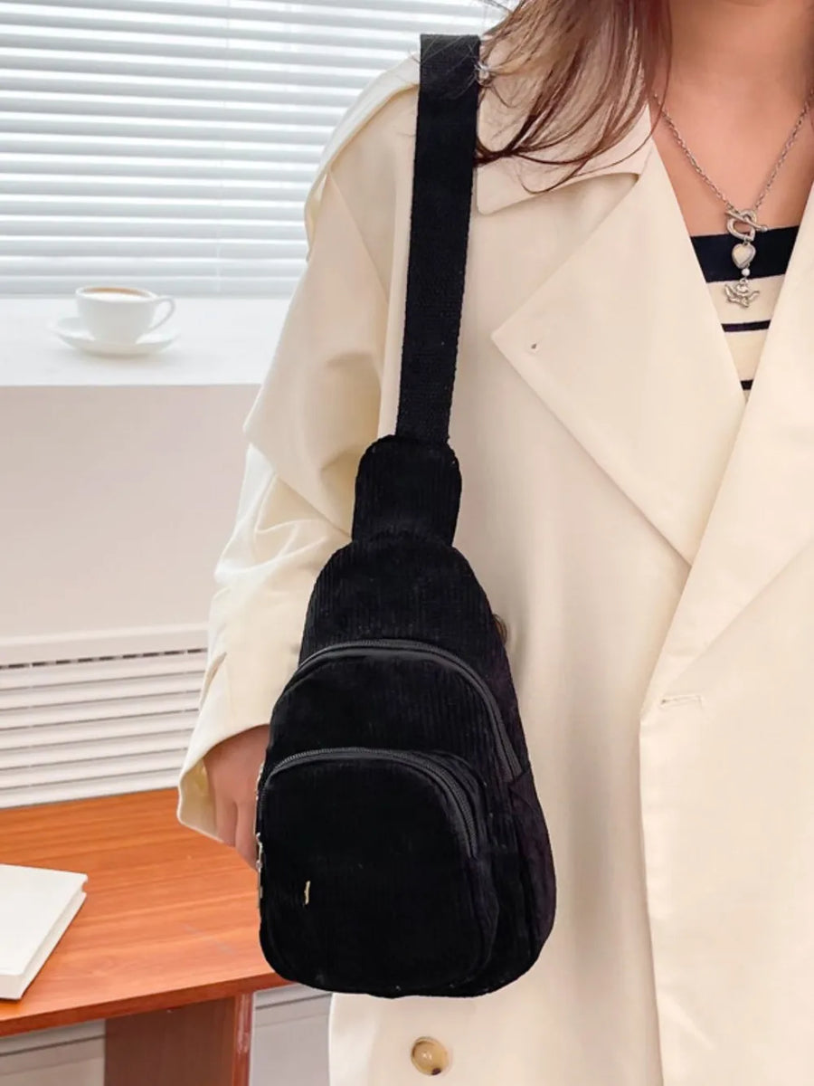 Black corduroy sling bag with zip pockets and adjustable strap.