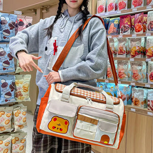 Cream travel bag with orange trim, gingham pattern, and cute bear applique.
