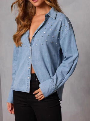 Light wash denim button-up shirt with pearl embellishments and long sleeves.