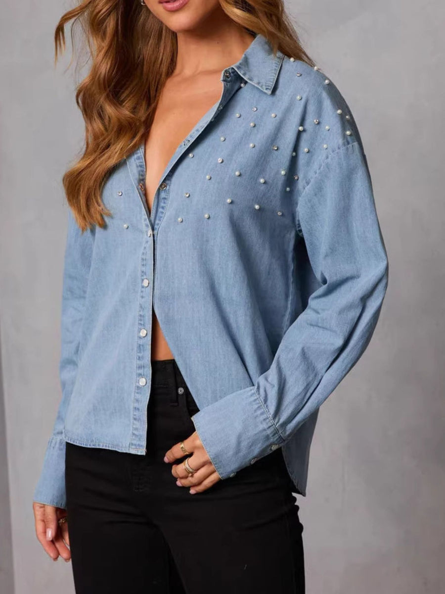 Light wash denim button-up shirt with pearl embellishments and long sleeves.