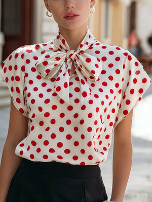 White polka dot shirt with red dots and a large bow tie neck, cap sleeves.