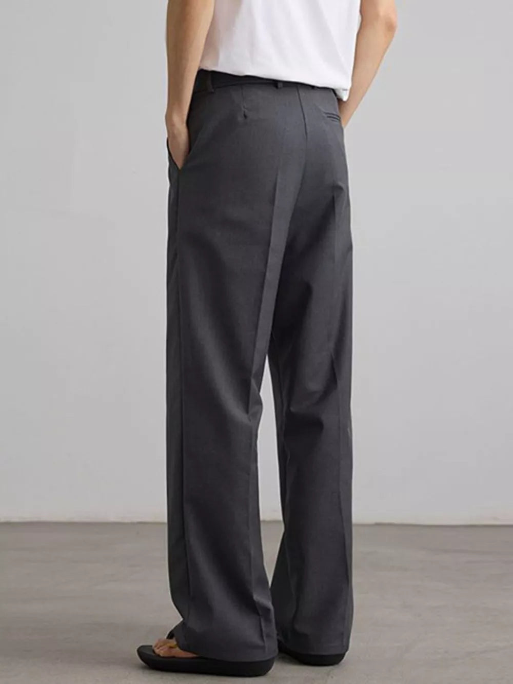 Grey pleated wide-leg trousers with a relaxed fit, shown from the back.