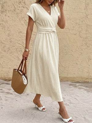 Beige cotton blend midi dress with V-neck, short sleeves, and twisted knot waist detail.