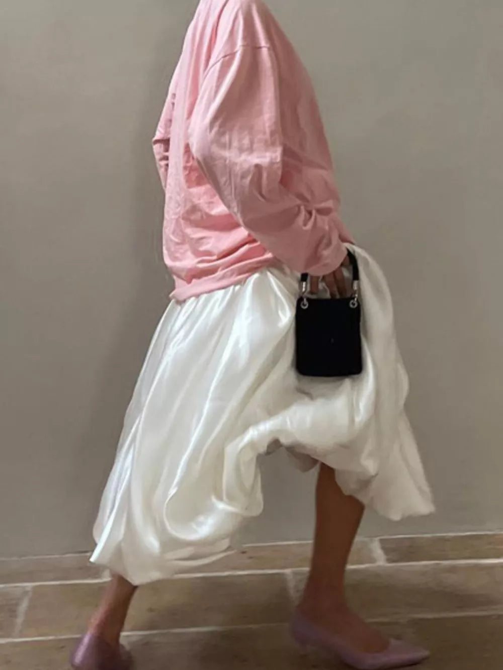 Pink long sleeve top and white satin midi skirt with a black handbag.