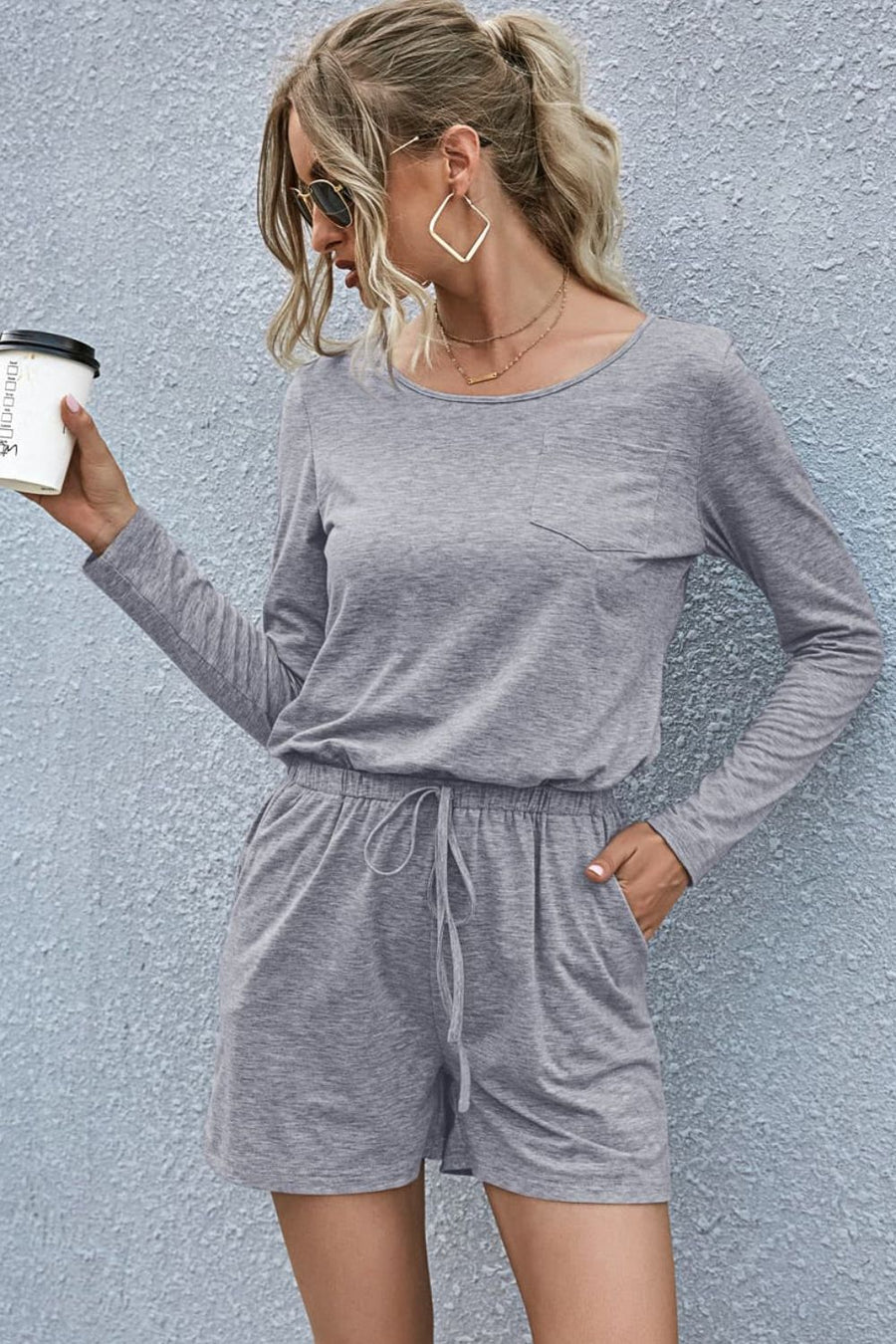 Gray jersey romper with long sleeves, chest pocket, drawstring waist, and pockets.