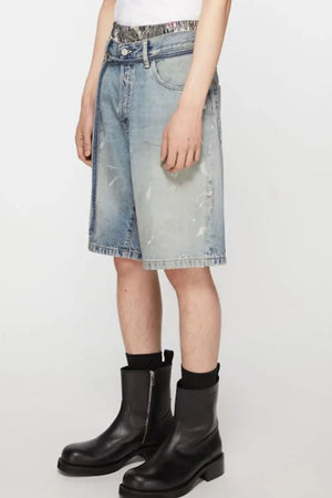 Distressed denim bermuda shorts in medium wash with white paint splatters and a tie belt.