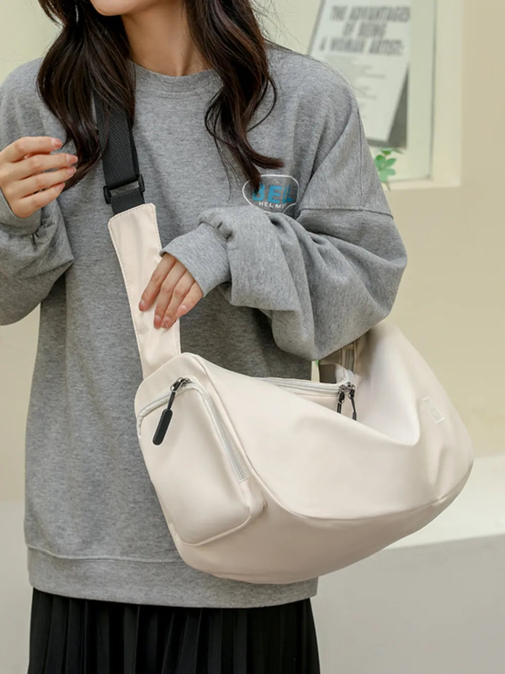 Slouchy crescent crossbody bag in beige with adjustable strap and zippered pockets.