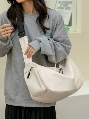 Slouchy crescent crossbody bag in beige with adjustable strap and zippered pockets.