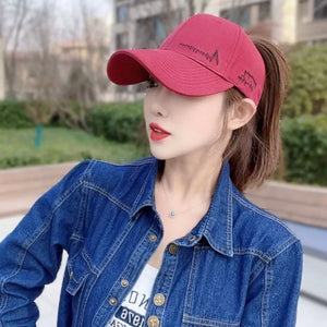 Red baseball cap with embroidered detail, worn by a woman in a denim jacket.