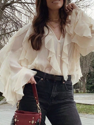 Beige sheer blouse with ruffles and long sleeves, V-neck, button front, styled with jeans.