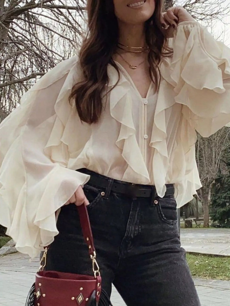Beige sheer blouse with ruffles and long sleeves, V-neck, button front, styled with jeans.
