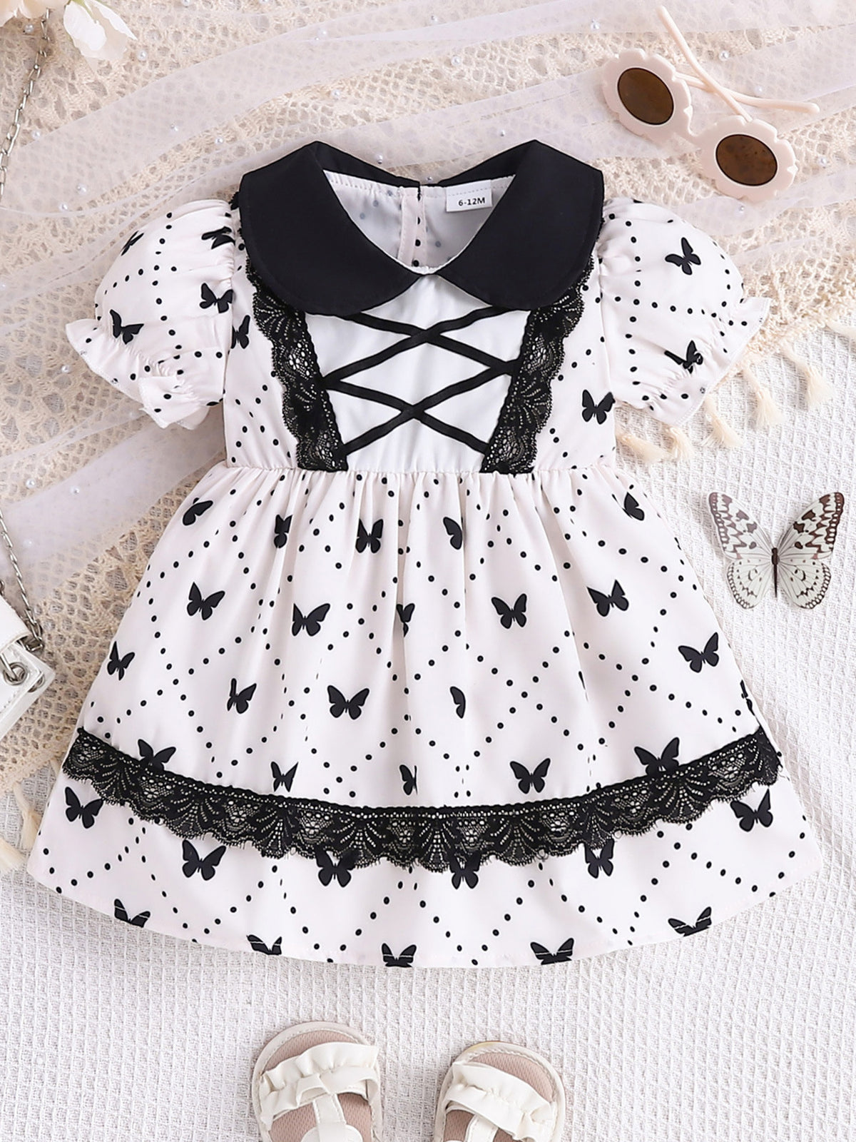 Baby dress with black collar, lace trim, and black butterfly print on white fabric.