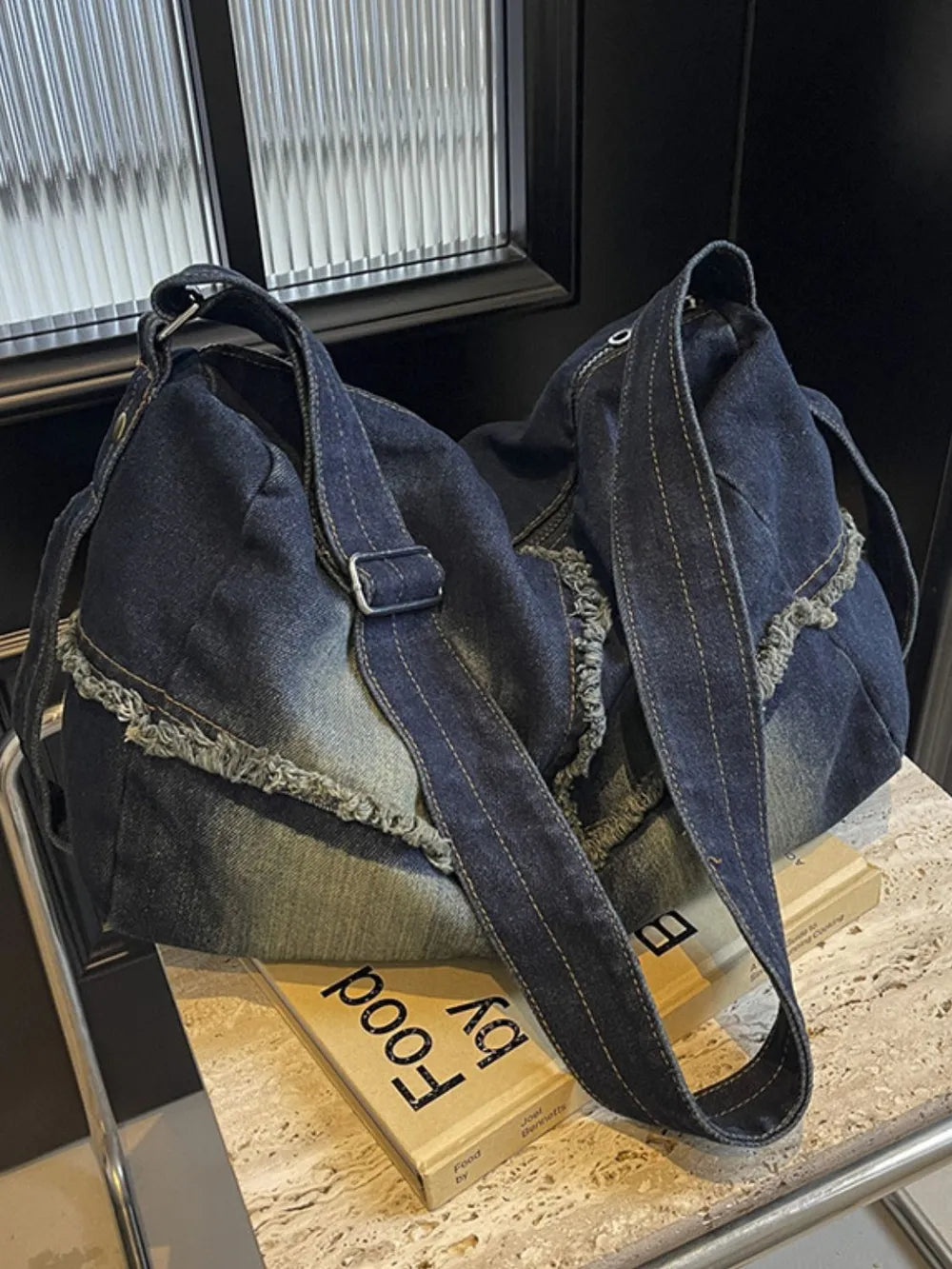 Frayed denim slouch crossbody bag in dark wash with adjustable strap and distressed details.