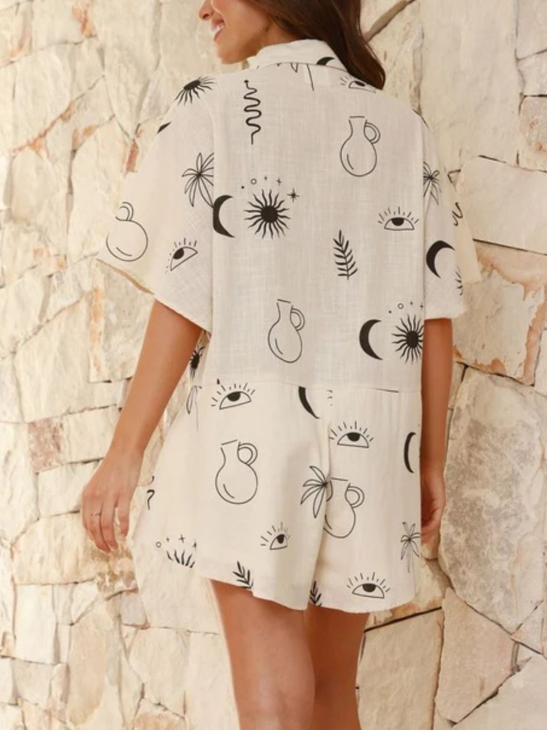 Beige linen romper with celestial print, short sleeves, and flared hem shorts.