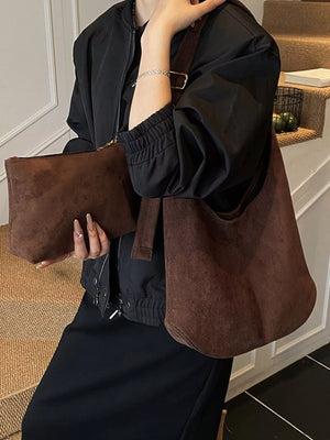 Large brown suede hobo bag with a matching clutch held by a woman in a black jacket.