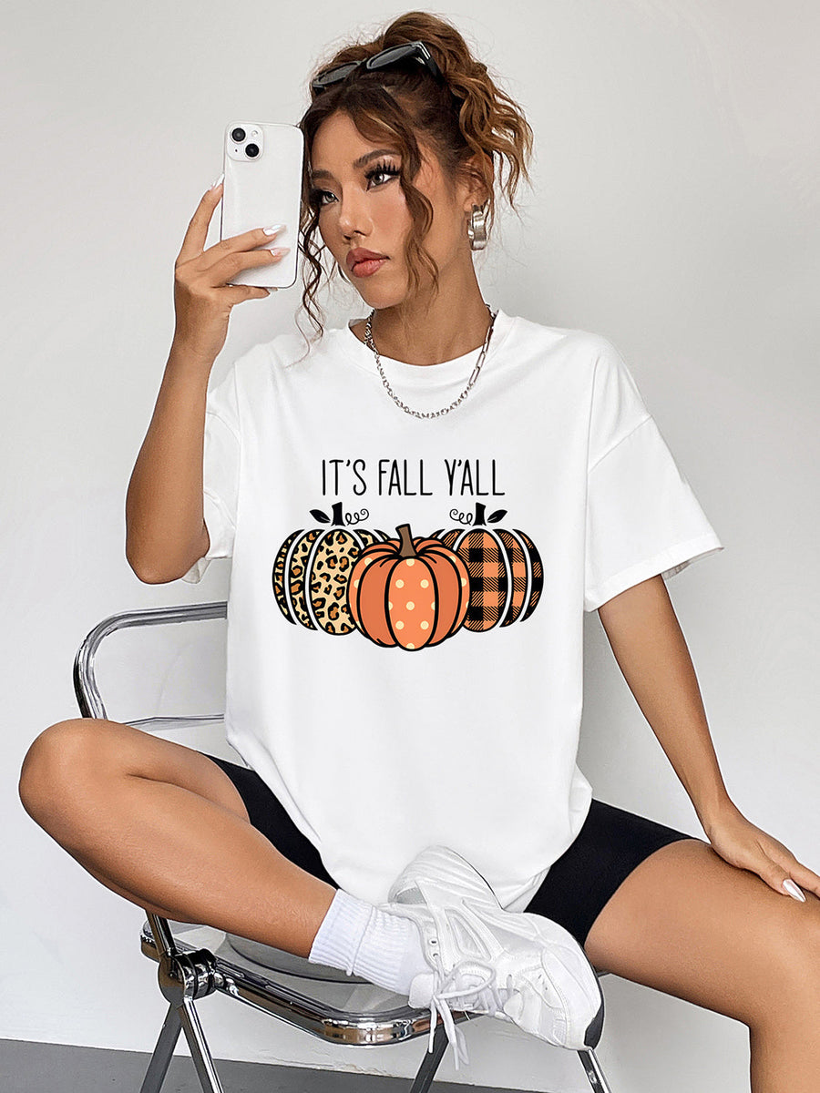 White graphic t-shirt with "IT'S FALL Y'ALL" and three pumpkins in leopard, polka dot, and plaid patterns.