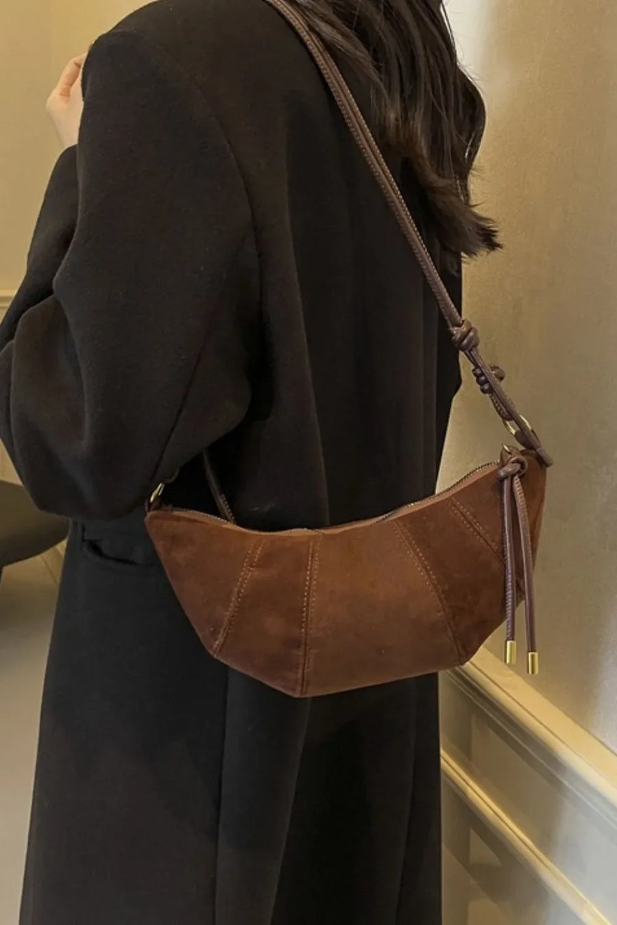 Brown suede crescent shoulder bag with knot detail and gold accents.