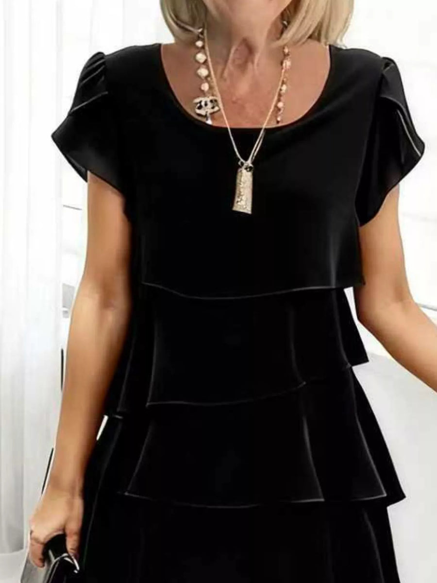 Black ruffled tiered dress with petal sleeves and scoop neck, styled with a long necklace.