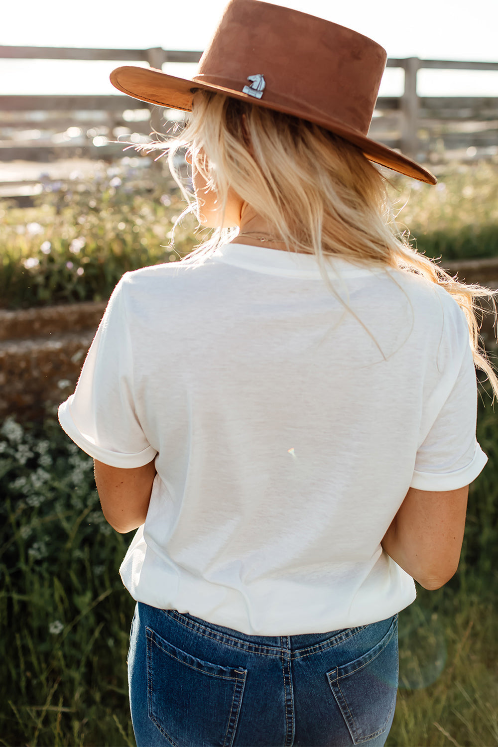 White graphic tee with rolled sleeves, styled with jeans and a brown hat.