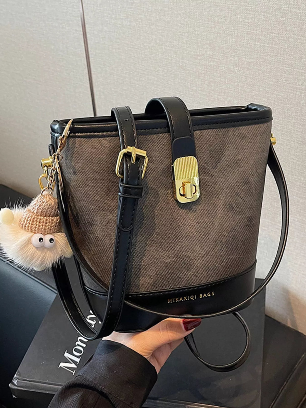 Elegant bucket bag in dark brown with black PU leather trim and gold hardware, featuring a playful charm.