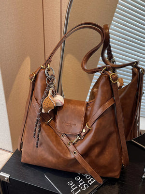 Brown PU leather hobo bag with decorative charms and adjustable strap.