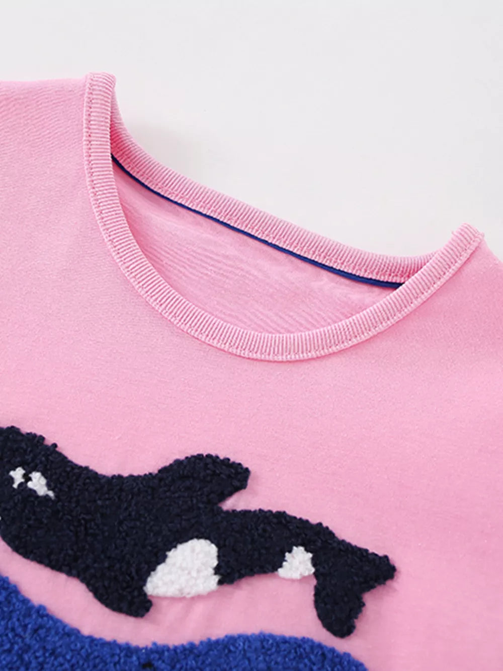 Pink cotton t-shirt with embroidered orca whale and blue waves detail.