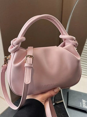 Pink ruched crossbody bag with knotted handles and gold buckle detail.