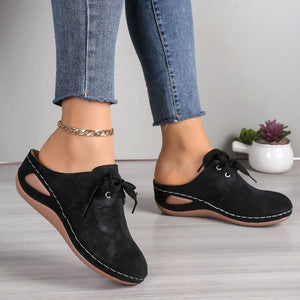 Black perforated lace-up mule flats with cutout sides and white stitching detail.
