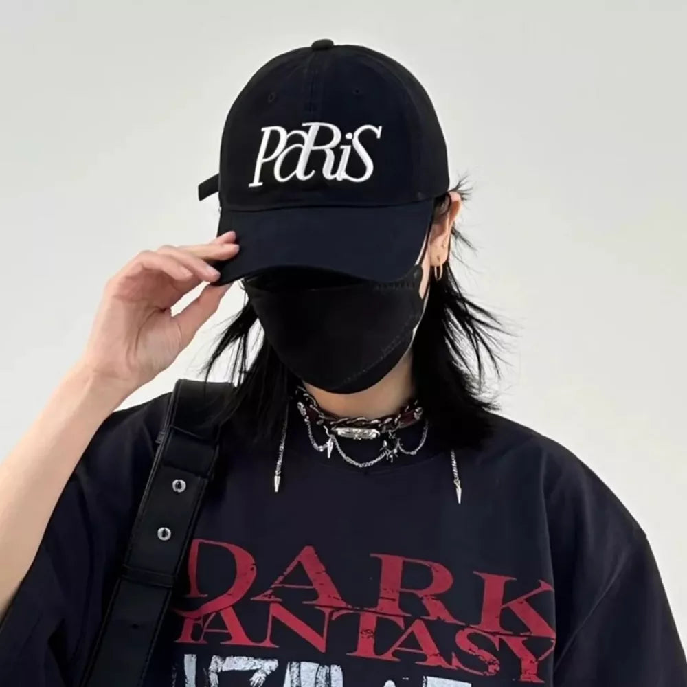 Black baseball cap with white Paris embroidery, styled with a black t-shirt and chain necklace.