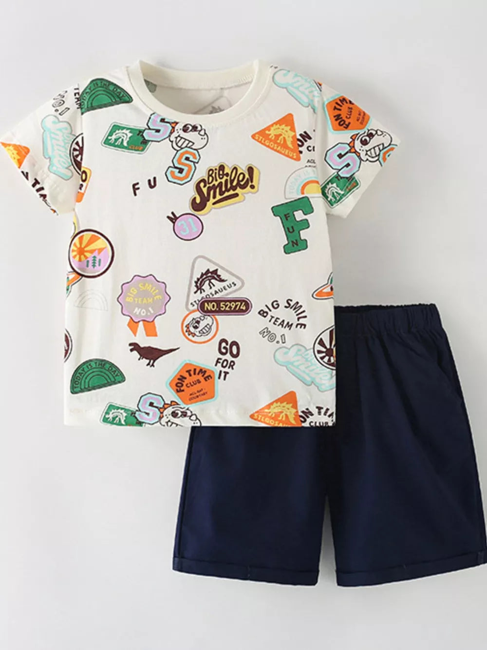 Toddler beige cotton t-shirt set with allover dinosaur patch graphic and navy shorts.