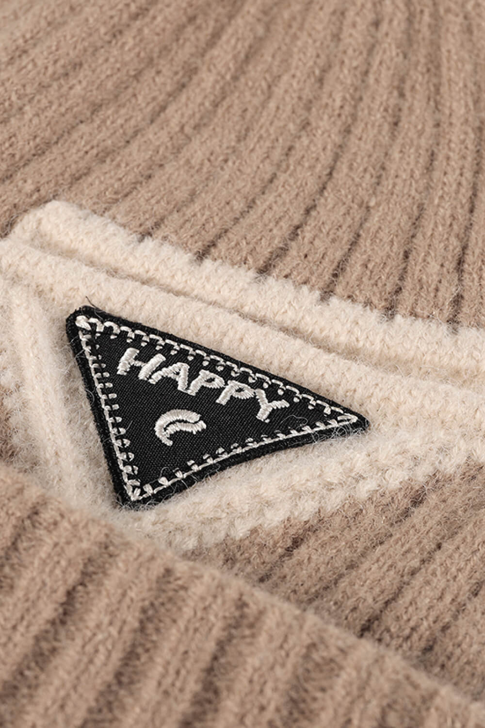 Ribbed acrylic beanie in beige and cream with a black "Happy" patch detail.