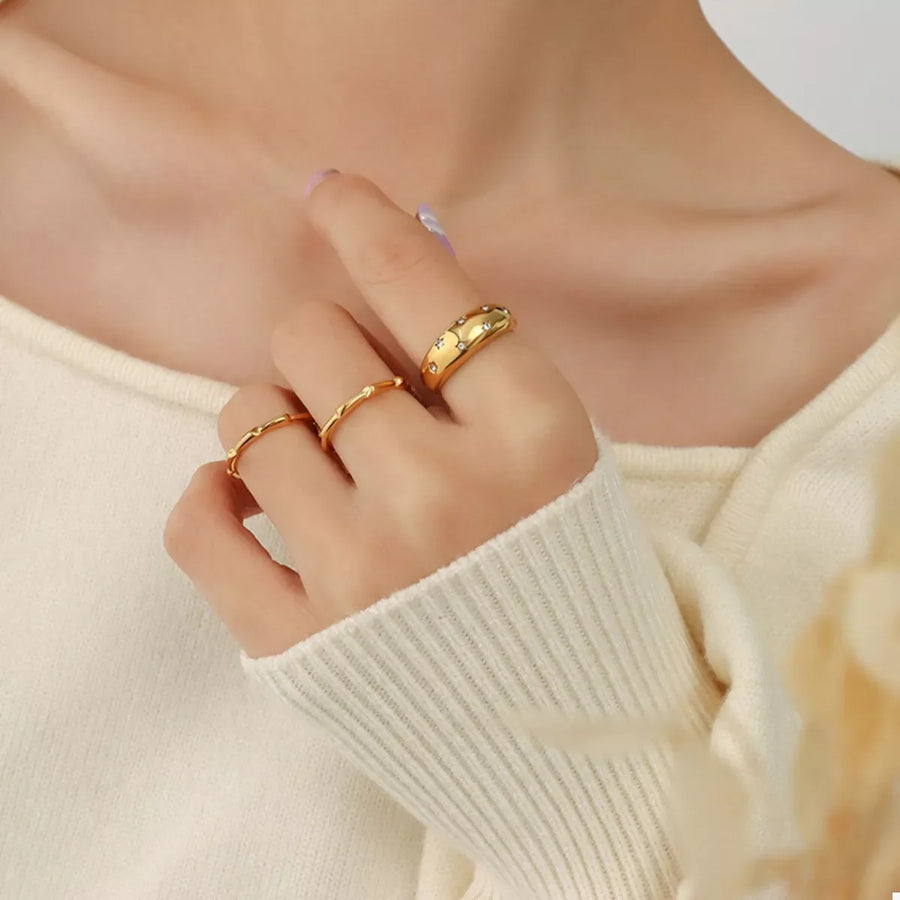 Gold rings with zircon studs and twisted bands, worn on a woman's hand.