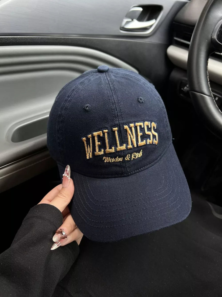 Navy blue cotton baseball cap with gold embroidered WELLNESS and Wisdom & Rich text.