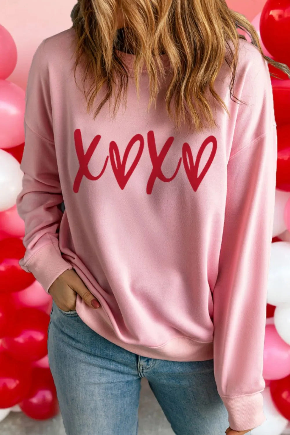 Blush pink sweatshirt with red XOXO graphic, crewneck, relaxed fit, long sleeves.