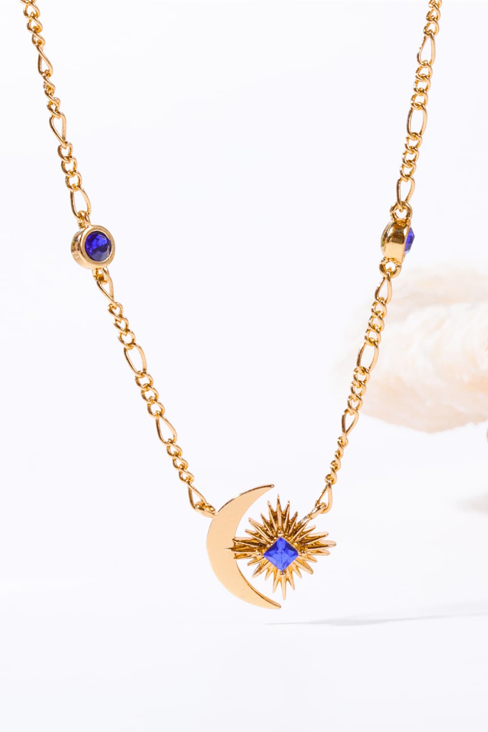 Gold celestial necklace with crescent moon, sunburst, and blue gems.