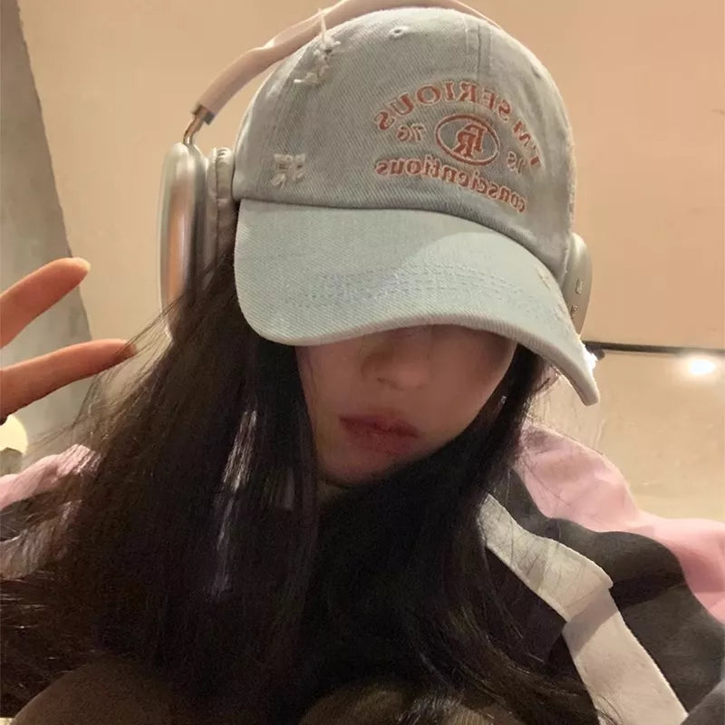 Light blue distressed baseball cap with embroidered text and logo, worn with headphones.