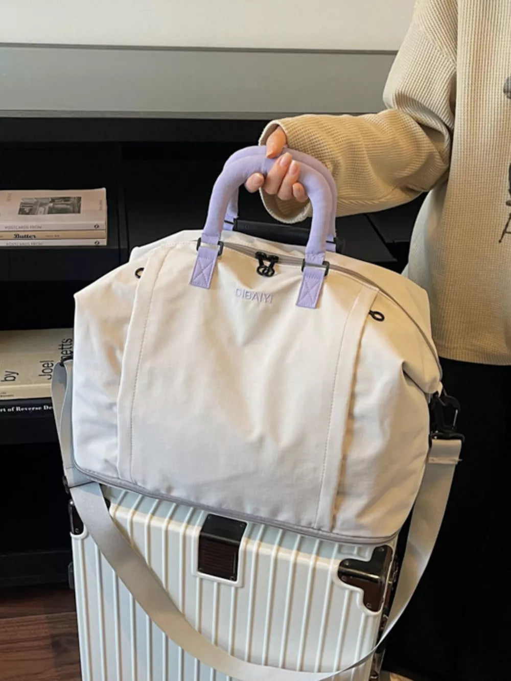 Sleek grey nylon travel bag with purple handles and adjustable strap, shown on a suitcase.