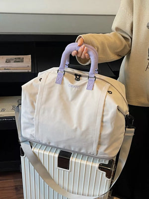 Sleek grey nylon travel bag with purple handles and adjustable strap, shown on a suitcase.