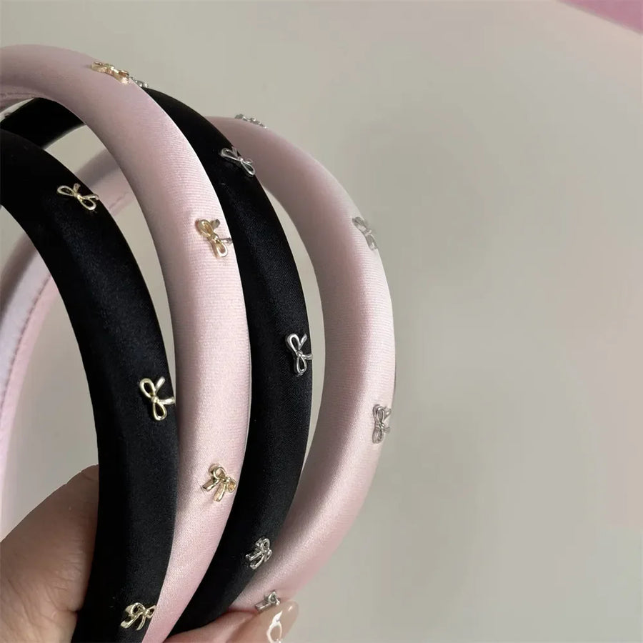Padded satin headbands in black and pink with gold and silver bow embellishments.