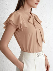 Tan tie-neck blouse with ruffle sleeves and lace trim, styled with white pants.
