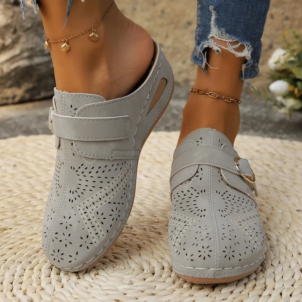 Gray laser-cut buckle mule wedges with perforated floral pattern and adjustable strap.