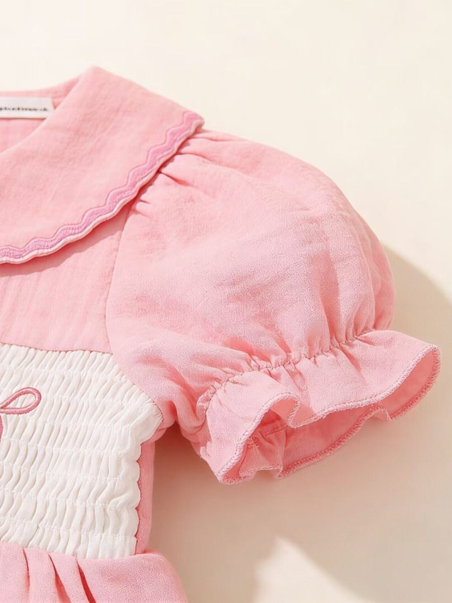 Pink baby dress with smocked bodice, puff sleeves, and embroidered teddy bear detail.