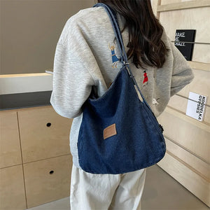 Denim hobo bag in medium blue with leatherette patch and adjustable strap.