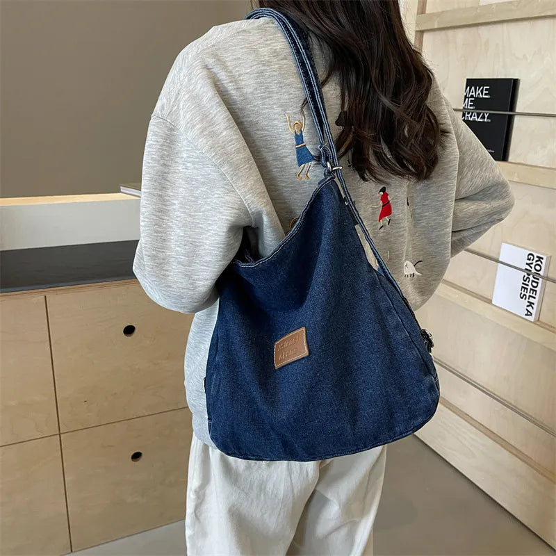 Denim hobo bag in medium blue with leatherette patch and adjustable strap.