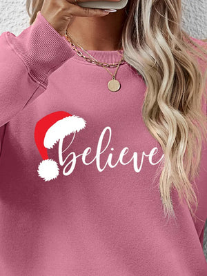 Blush pink raglan sweatshirt with "believe" graphic and Santa hat detail.