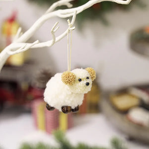Woolly sheep ornament with pom-pom ears, black eyes, and brown feet, hanging from a branch.